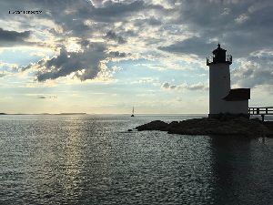 The Annisquam Lighthouse at sunset with a sailboat in the background.