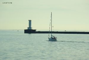 A sailboat passes by the lighthouse.